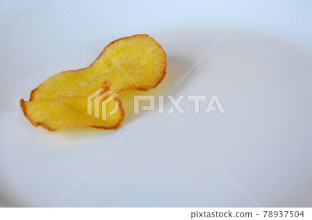 Dried and fried cassava slices place on white plate isolated on wood texture background. This is local Malaysian traditional junk food call Kerepek Ubi.  78937504