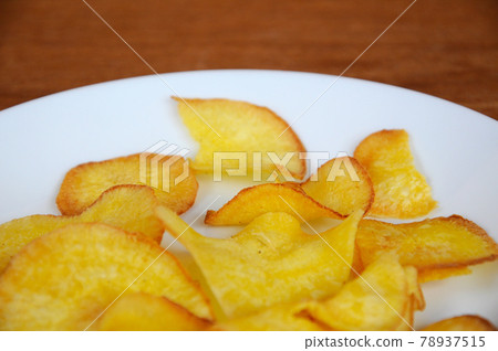 Dried and fried cassava slices place on white plate isolated on wood texture background. This is local Malaysian traditional junk food call Kerepek Ubi.  78937515