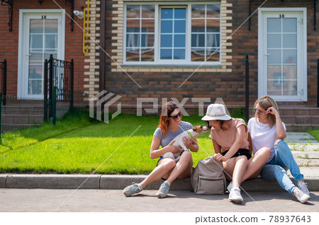 Three Caucasian women and a dog go on a trip. The girls are sitting on the curb with suitcases and waiting for a taxi. Summer vacation concept together with girlfriends 78937643