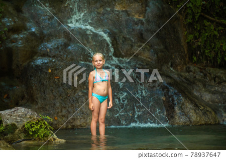 a little girl in a swimsuit at a waterfall in the jungle. Nature trip near a beautiful waterfall, Turkey 78937647