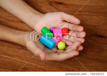 Children hand holding colorful of rubber cube and other shapes on wood texture background. Children hand holding colorful of rubber cube and other shapes on wood texture background. 78938525