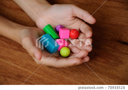 Children hand holding colorful of rubber cube and other shapes on wood texture background. Children hand holding colorful of rubber cube and other shapes on wood texture background. 78938528