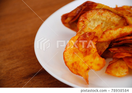 Dried and fried cassava slices mixed with spicy chili sauce place on white plate isolated on wood texture background. This is local Malaysian traditional junk food also call as Kerepek Ubi.    78938584