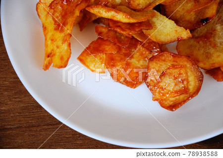 Dried and fried cassava slices mixed with spicy chili sauce place on white plate isolated on wood texture background. This is local Malaysian traditional junk food also call as Kerepek Ubi.    78938588