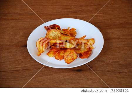 Dried and fried cassava slices mixed with spicy chili sauce place on white plate isolated on wood texture background. This is local Malaysian traditional junk food also call as Kerepek Ubi.    78938591
