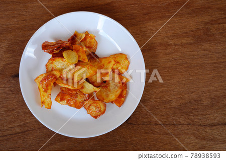 Dried and fried cassava slices mixed with spicy chili sauce place on white plate isolated on wood texture background. This is local Malaysian traditional junk food also call as Kerepek Ubi. Dried and fried cassava slices mixed with spicy chili sauce place on white plate isolated on wood texture background. This is local Malaysian traditional junk food also call as Kerepek Ubi. 78938593