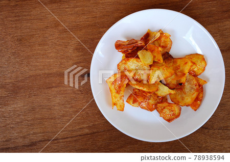 Dried and fried cassava slices mixed with spicy chili sauce place on white plate isolated on wood texture background. This is local Malaysian traditional junk food also call as Kerepek Ubi.    78938594