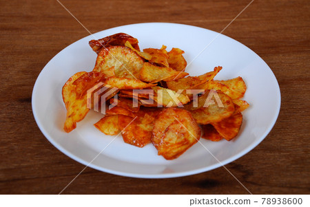 Dried and fried cassava slices mixed with spicy chili sauce place on white plate isolated on wood texture background. This is local Malaysian traditional junk food also call as Kerepek Ubi. Dried and fried cassava slices mixed with spicy chili sauce place on white plate isolated on wood texture background. This is local Malaysian traditional junk food also call as Kerepek Ubi. 78938600