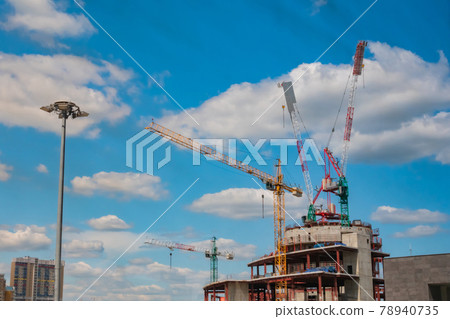 Yellow tower cranes and unfinished building construction against blue sky 78940735