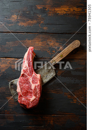 Raw Cowboy steak on meat cleaver. Organic farm marbled prime beef. Dark wooden background. Top view. Copy space. Nobody Noone. Raw Cowboy steak on meat cleaver. Organic farm marbled prime beef. Dark wooden background. Top view. Copy space. Nobody Noone. 78941305