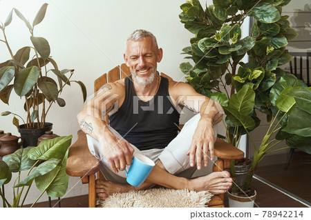 Happy middle aged caucasian man drinking morning coffee while sitting in lotus pose on the terrace of his modern flat Happy middle aged caucasian man drinking morning coffee while sitting in lotus pose on the terrace of his modern flat 78942214