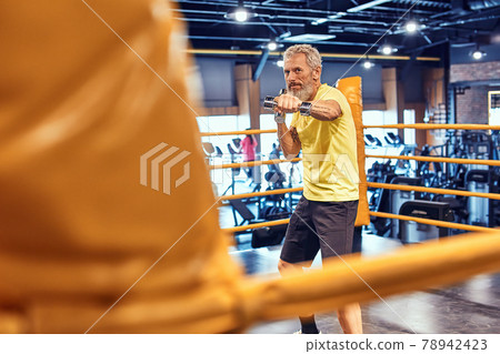 Best cardio. Athletic mature man in sportswear boxing while standing on the ring at gym Best cardio. Athletic mature man in sportswear boxing while standing on the ring at gym 78942423