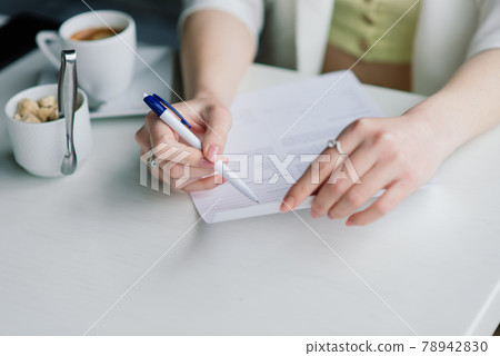 Young woman in white jacket working in cafe with papers, drinking coffee 78942830