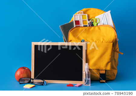 Yellow backpack and chalk board on blue background Yellow backpack and chalk board on blue background 78943190
