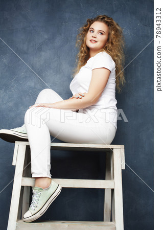 young pretty hipster girl with curly blond hair posing emotonal on blue wall background, lifestyle people concept 78943312