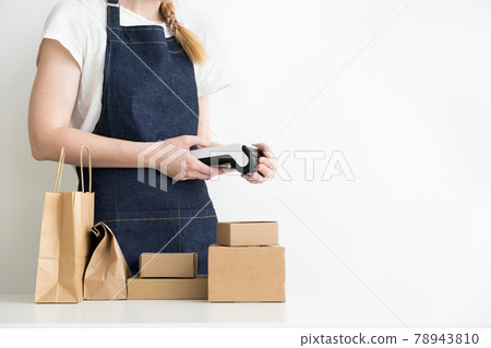 Woman holding modern payment terminal in hands with carton boxes, cardboard packages and kraft bag on the table Woman holding modern payment terminal in hands with carton boxes, cardboard packages and kraft bag on the table 78943810