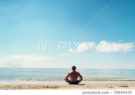 Man meditates on the sandy beach view from the back Man meditates on the sandy beach view from the back 78944470