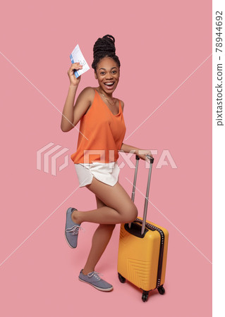 Dark-skinned woman holding a suitcase and a plane ticket 78944692