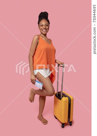 Dark-skinned woman holding a suitcase and a plane ticket 78944695