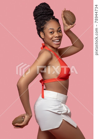 Dark-skinned woman holding coconuts and having fun 78944734