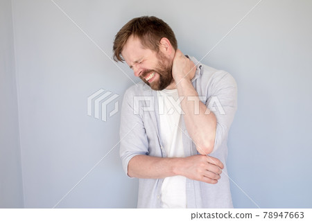 Caucasian man is experiencing severe pain in neck, he massages the sore spot with hand and bares 78947663