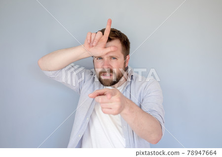Annoyed Caucasian man in casual clothes insults someone with a loser gesture, fingers on forehead 78947664
