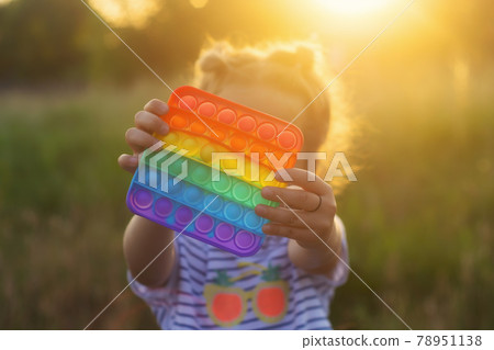The child plays with a colorful rainbow game of poppit. Silicone fidget close-up. The child plays with a colorful rainbow game of poppit. Silicone fidget close-up. 78951138
