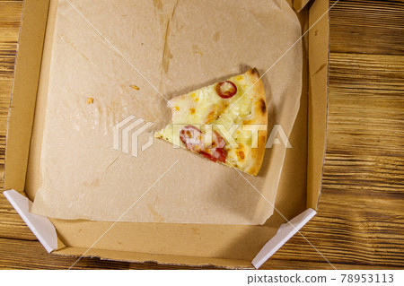 Bitten slice of pizza in cardboard box on a wooden table. Top view. Concept for home delivery of food, fast food, delivery of pizza 78953113