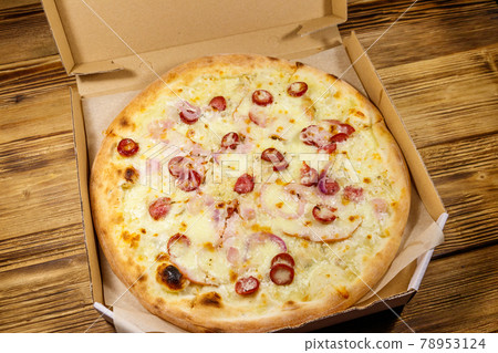 Delicious fresh pizza in cardboard box on a wooden table. Concept for home delivery of food, fast food, delivery of pizza Delicious fresh pizza in cardboard box on a wooden table. Concept for home delivery of food, fast food, delivery of pizza 78953124
