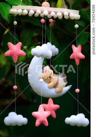 Dreamy baby crib mobile close up, hangs over the baby bed, cute bear sleeping on the moon, stuffed fluffy felt handmade cot toy for newborn babies. Dreamy baby crib mobile close up, hangs over the baby bed, cute bear sleeping on the moon, stuffed fluffy felt handmade cot toy for newborn babies. 78954886