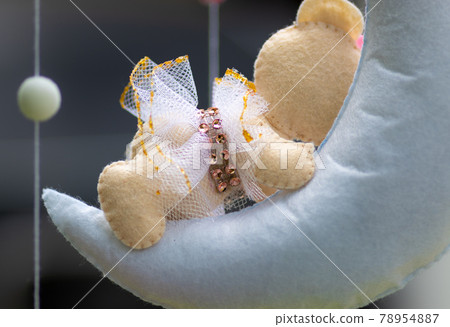 Dreamy baby crib mobile close up, hangs over the baby bed, cute bear sleeping on the moon, stuffed fluffy felt handmade cot toy for newborn babies. Dreamy baby crib mobile close up, hangs over the baby bed, cute bear sleeping on the moon, stuffed fluffy felt handmade cot toy for newborn babies. 78954887