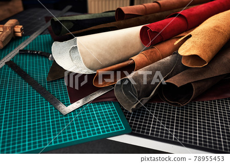 Samples of genuine leather of different colors on a craft table, surrounded by tools in a leather dressing and processing workshop. Samples of genuine leather of different colors on a craft table, surrounded by tools in a leather dressing and processing workshop. 78955453