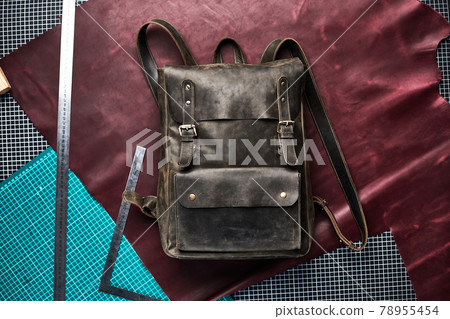 Unisex brown leather backpack on a craft background in the workshop on the table, a handmade leather backpack. Unisex brown leather backpack on a craft background in the workshop on the table, a handmade leather backpack. 78955454