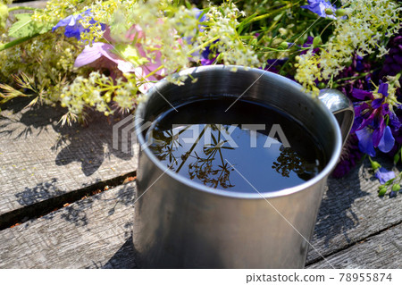 Steel travel cup of tea near the flowers stands on a gray wooden table 78955874