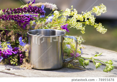 Hiking steel mug stands on a gray wooden table near the flowers 78955878