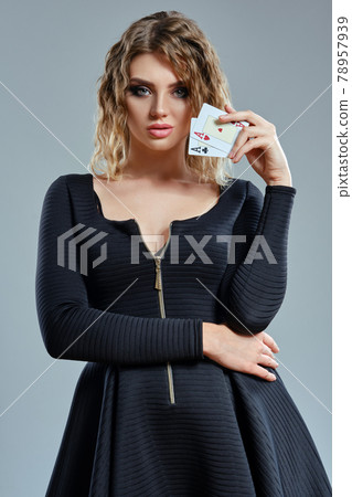 Blonde girl in black dress showing two aces, posing against gray background. Gambling entertainment, poker, casino. Close-up. 78957939