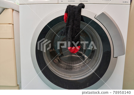 A clean black sock hangs on the door of the washing machine 78958140