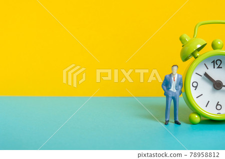 Man's dummy next to a green vintage clock on a yellow background and right side. 78958812
