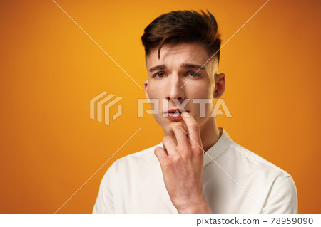 Frustrated and nervous young man biting nail against yellow background Frustrated and nervous young man biting nail against yellow background 78959090