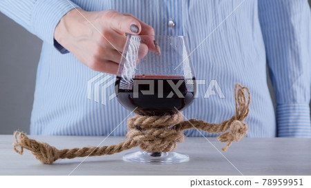 female hand shows the sign CANNOT, STOP on a wine glass, tied with a jute rope. The concept of female hand shows the sign CANNOT, STOP on a wine glass, tied with a jute rope. The concept of 78959951