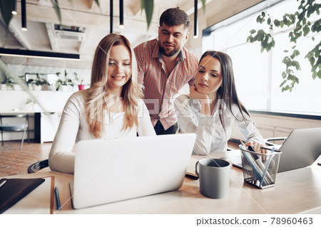 Two female and one male business partners looking at computer screen and discussing their project Two female and one male business partners looking at computer screen and discussing their project 78960463