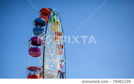 A large Ferris wheel against a blue sky. Booths with people go up. A large Ferris wheel against a blue sky. Booths with people go up. 78962199