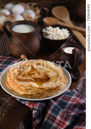 A stack of thin pancakes with honey on a wooden board. 78964649