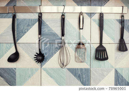 Kitchen spatulas handing on railing on a tiled wall with blue geometric pattern Kitchen spatulas handing on railing on a tiled wall with blue geometric pattern 78965001