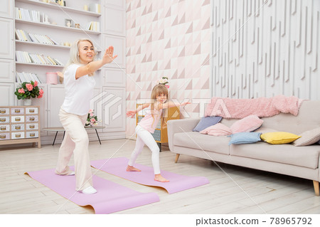 Smiling blond mother on yoga mat with cute playful daughter do exercises. 78965792