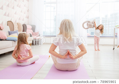 Smiling blond mother on yoga mat with cute playful daughter do exercises. Smiling blond mother on yoga mat with cute playful daughter do exercises. 78965901