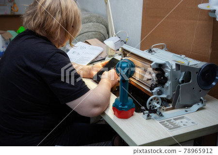 Woman tilts the sewing machine on its side and reads the repair instructions 78965912