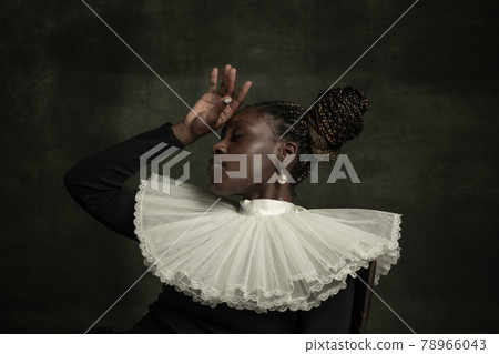 Portrait of medieval African young woman in black vintage dress with big white collar posing isolated on dark green background. Terrible headache Portrait of medieval African young woman in black vintage dress with big white collar posing isolated on dark green background. Terrible headache 78966043