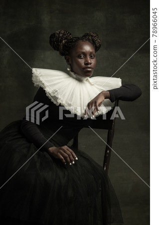 Portrait of medieval African young woman in black vintage dress with big white collar posing isolated on dark green background. Portrait of medieval African young woman in black vintage dress with big white collar posing isolated on dark green background. 78966045