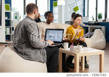 Businessman holding laptop with financial ghraphics while diverse employees talking 78967585